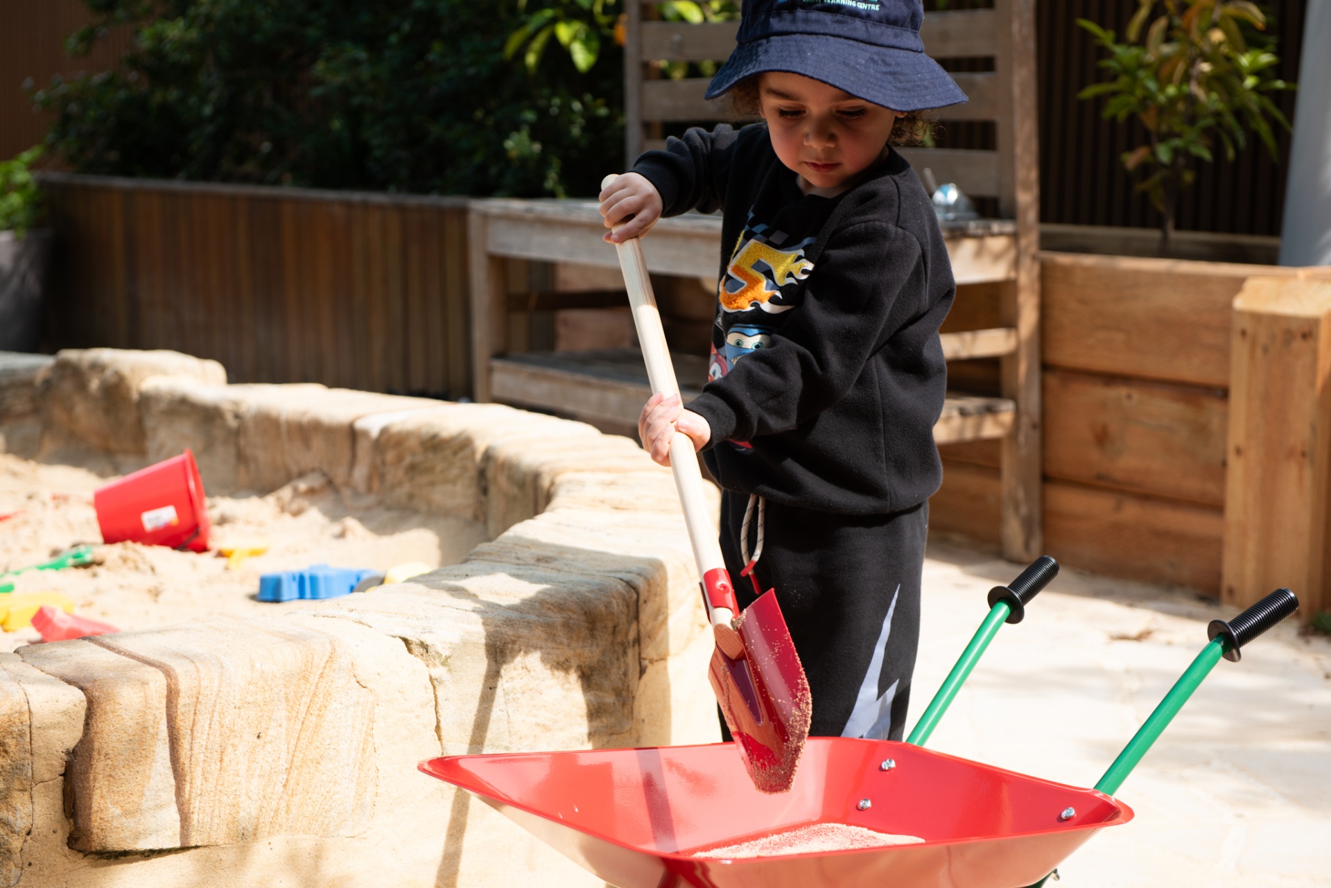 Child shovelling sand into a wheelbarrow